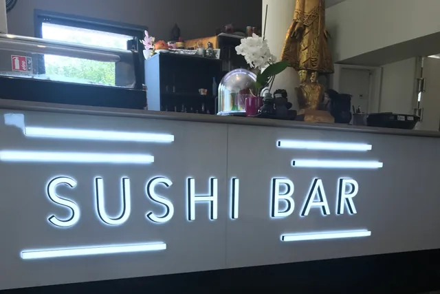 Le comptoir du bar à sushis, son enseigne lumineuse et une statue dorée